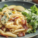 A photo of a pasta recipe on a plate containing penne, blue cheese and bacon bits